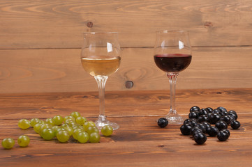 Red and white wine glasses and grape on wooden table