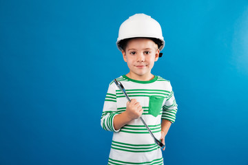 Pleased young boy in protective helmet posing with wrench