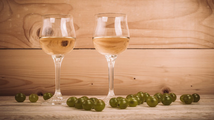 Two glasses of white wine and grapes on wooden table