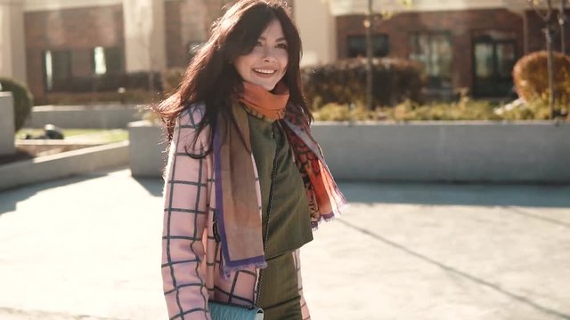 charming young woman walks through the autumn city in a coat and smiles. cute girl on a background of modern architecture. slow motion