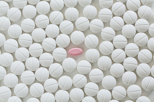 One Pink Pill Surrounded By White Prescription Pills On White Background