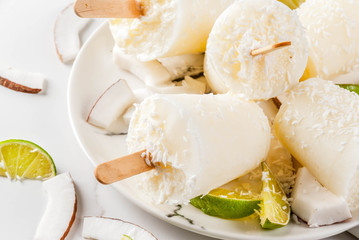 Summer desserts. Vegan diet food. Coconut and lime home fruit ice cream popsicles on a stick. On white marble table, copy space