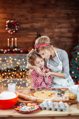 Merry Christmas and Happy Holidays. Family preparation holiday food. Mother and daughter cooking cookies in New Year interior with Christmas tree.