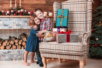 Beautiful happy laughing children in New Year interior with Christmas tree and fireplace. Brother hugging his sister. The concept of a family holiday