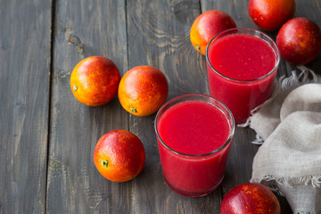 Freshly squeezed juice of blood oranges in glasses with whole fresh oranges on a wooden table, selective focus, free space