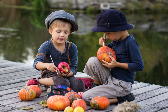 Two cheerful boys paint small Halloween pumpkins