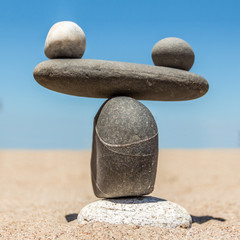 Figure in the form of weights from sea stones on a sandy beach. A square picture.