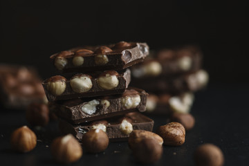 Chocolate bar pieces and nuts on dark slate background with copy space. Chocolate background. Top view. Toned