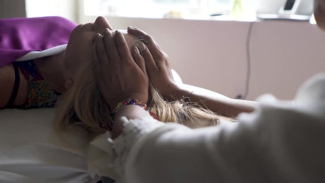 Very tight shot of a polarity therapist with her hands on her patient&rsquo;s head feeling her energy.