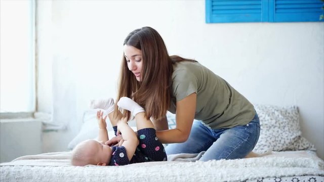 A young woman who plays with her daughter kisses and tickles the girl, they spend a day off together in bed, mom shows her love, the child enjoys childhood