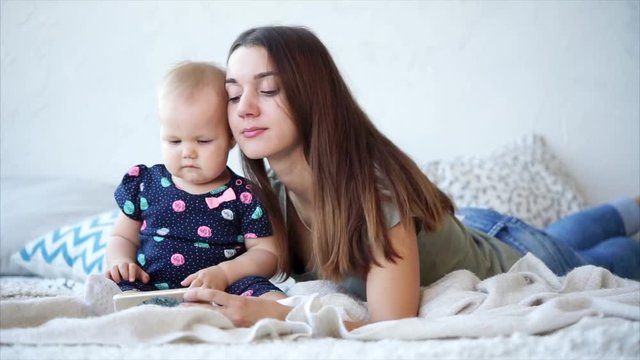 An attractive and young woman is spending a day off together with her daughter, a lady and a child are watching a cartoon on a mobile phone, mom is enjoying motherhood