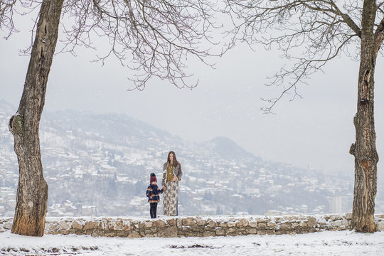 Beautiful pregnant woman with her little son outside while snowing