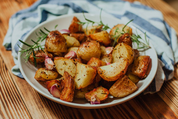 Roasted potato in white plate on wooden background with rosemary and garlic