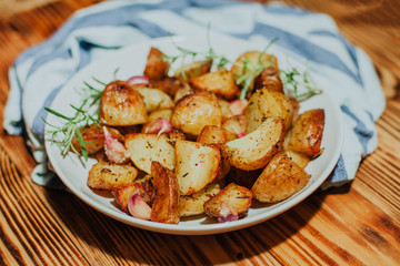 Roasted potato in white plate on wooden background with rosemary and garlic