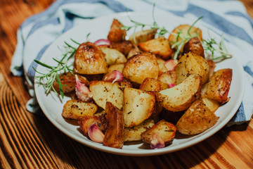 Roasted potato in white plate on wooden background with rosemary and garlic