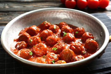 Saucepan with delicious meatballs in tomato sauce on table