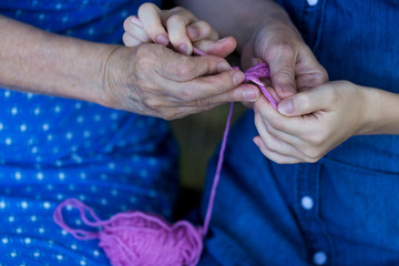 Grandmother teaches her granddaughter to crochet. Hands of elderly woman and young girl.