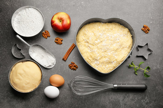 Raw dough in baking pan and ingredients on kitchen table