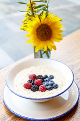 Oatmeal with berries with a yellow flower on the background of the rainy window.