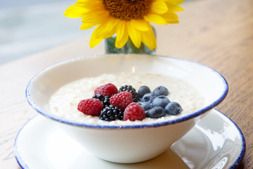 Oatmeal with berries with a yellow flower on the background of the rainy window.