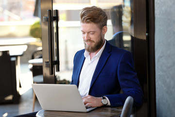 Fototapeta premium Smiling young entrepreneur working on laptop in cafe, business communication and remote work lifestyle