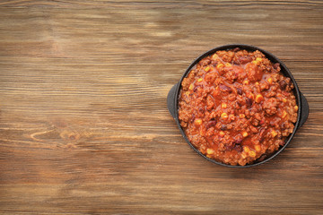 Chili con carne in frying pan on wooden background