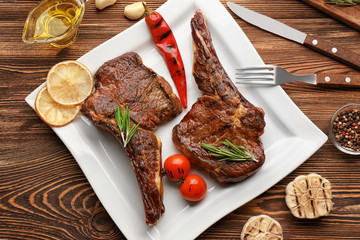 Plate with delicious grilled steaks on wooden table