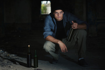 Man sitting with bottle of alcohol in abandoned building