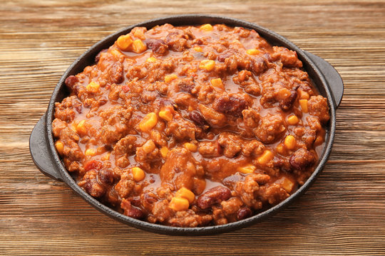 Chili con carne in frying pan on wooden background