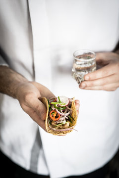 Chef holding in one hand a taco  and the other a shot of mezcal