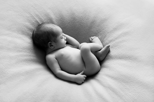 Beautiful naked newborn baby boy sleeping peacefully as if he would still be in womb.