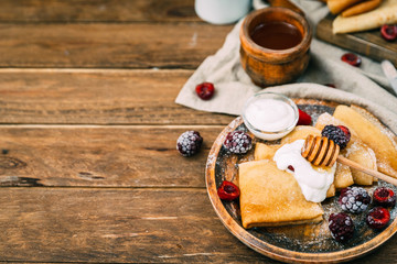 pancakes with berries, jam and honey on wooden table