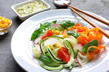 Plate with raw vegetable spaghetti and chopsticks on grunge background