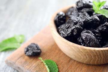 Bowl with tasty dried plums on table, closeup