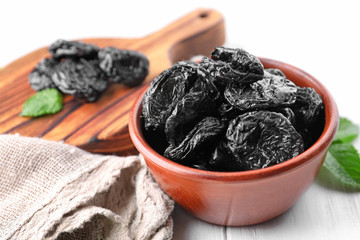 Bowl with tasty dried plums on white background