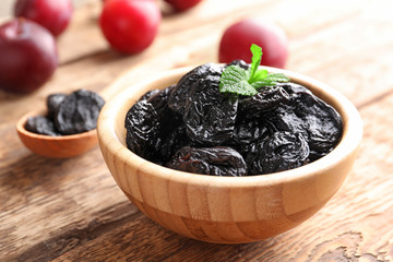 Bowl with tasty dried plums on table