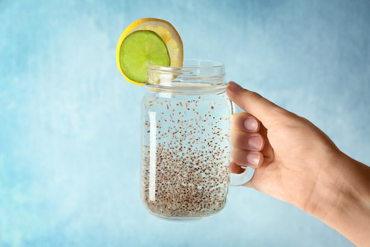 Woman holding mason jar of water with chia seeds on light background