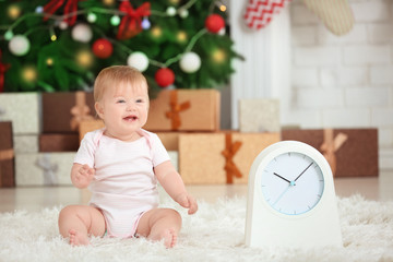 Adorable baby with clock in decorated room. Christmas countdown concept