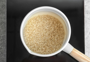 Saucepan with raw rice and water in kitchen