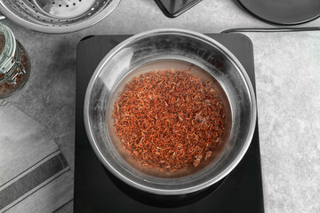 Bowl with raw rice and water in kitchen