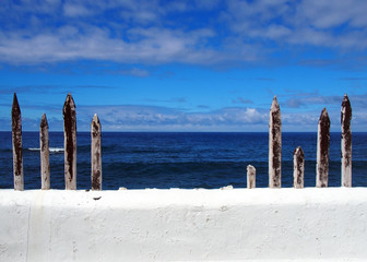 white painted wall with blue sea to the horizon with summer sky and clouds with old wooden fence posts