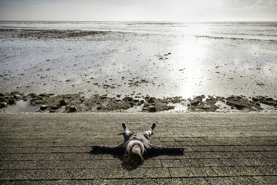 Woman lays down on a steep dyke in front of the north sea.