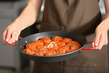 Woman holding pan with tasty sausage balls in kitchen, closeup