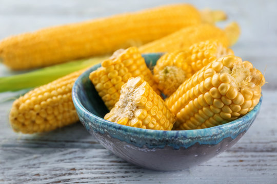 Bowl and fresh corn cobs on wooden table