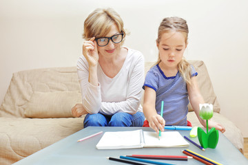 Fototapeta premium Cute little girl and her grandmother drawing in notebook on table