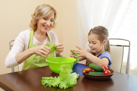 Cute little girl and her grandmother cooking on table