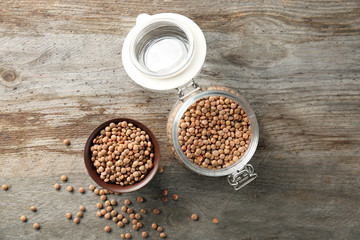 Jar and bowl with brown lentils on wooden table
