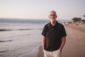 Content middle aged, retired man smiling outside on ocean beach at sunset