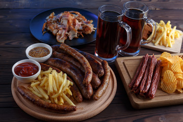 Appetizing beer snacks set. Top view on table with salami, grilled sausages and french fries served with spicy tomato sauce, mustard and dark beer, free space. Oktoberfest food, pub concept