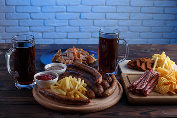 Appetizing beer snacks set. Pork slices, grilled sausages and french fries served with spicy tomato sauce, mustard and dark beer in mugs, free space. Oktoberfest food, pub concept